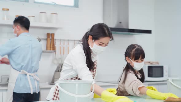 Asian young family wearing face mask due to Covid and teaching their daughter clean kitchen counter