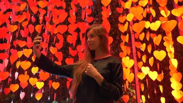Girl Blogger with Mobile Phone Going Through Decoration with Red Hanging Hearts
