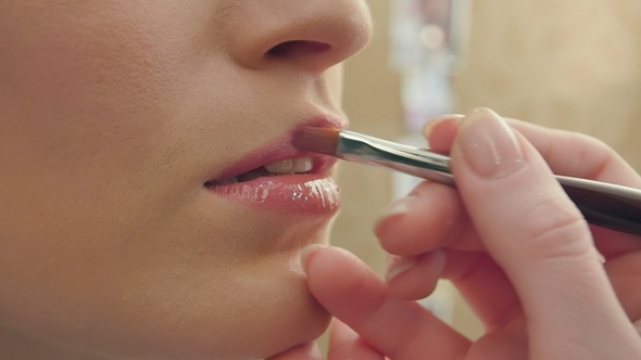 Makeup artist uses brush to apply lip gloss to model lips