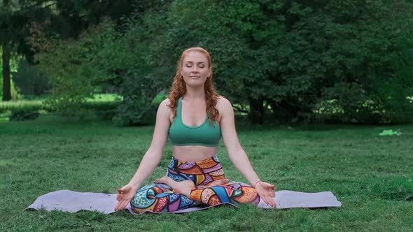 Young Woman Meditates in Lotus Pose in Park. Female Doing Yoga Outdoors.