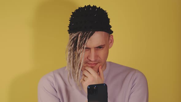 Young Thoughtful Man Browsing Mobile Phone on Yellow Background