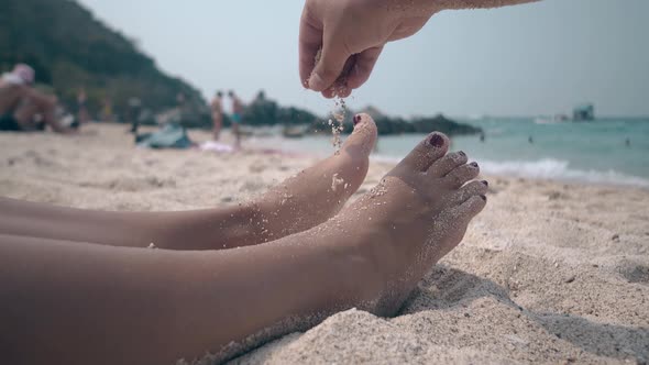 Man Sprinkles Pinch of Sand on Woman Legs Lying on Beach