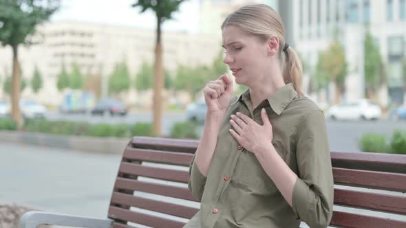 Sick Woman Coughing while Sitting on Bench Outdoor
