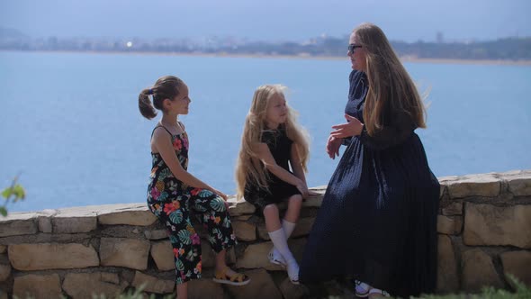 Family of a Woman and Two Daughters Sitting on the Stone Fencing By the Sea