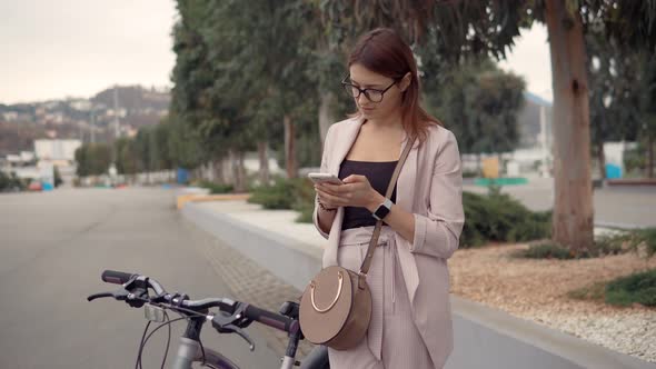 Charming Girl Is Reading and Sending Messages Standing Outdoors in City