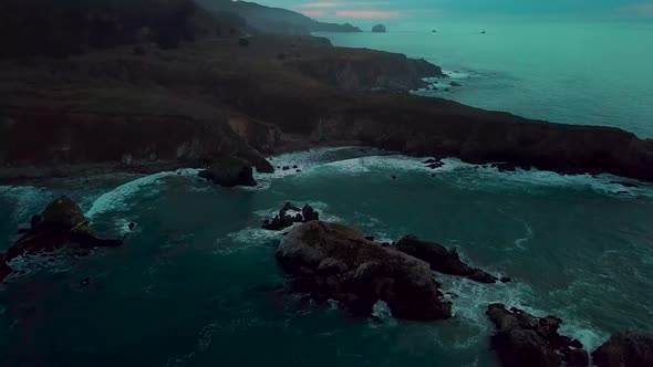 Fast dolly out reveal of huge ocean cliff peninsula eroded by crashing waves at dusk at Sand Dollar