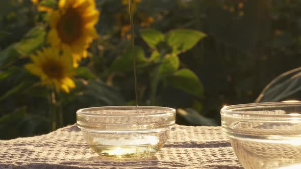 Sunflower Oil Poured In Glass Bowl On Field Of Sunflower Flowers. Oil Is Poured In Bowl In Trickle