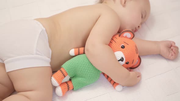 Toddler 12-17 months old sleeps in bed hugging a knitted tiger toy. Top view