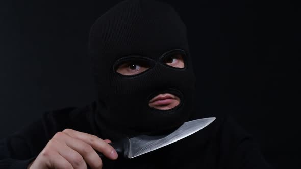 A criminal in a mask with a knife, a crazy maniac, touching his face with a knife in masks