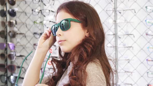 Little Cute Girl Trying on Sunglasses at the Eyewear Store