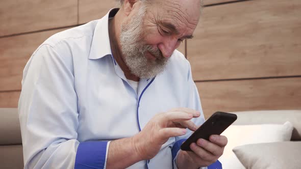 Happy bearded senior elderly 70s man user holding smart phone watching mobile video calling online l