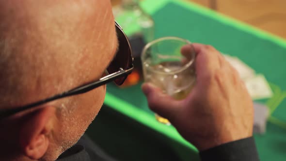 A Risky Gambler at the Card Table Takes a Sip of Whiskey Closeup While Playing