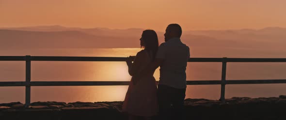 Young couple watching sunset above the lake from the viewing point, Medium shot