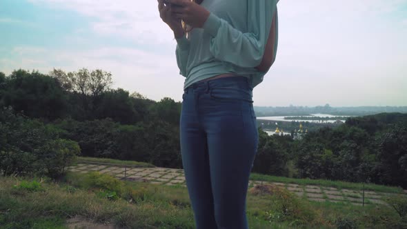 Young Stylish Girl Standing on a Hill and Gaining a Message on the Phone