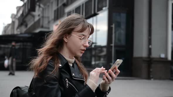 Beautiful Girl Student Writes with a Backpack Writes a Message on the Phone