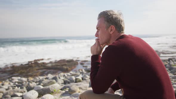 Caucasian man enjoying free time by sea on sunny day sitting and thinking