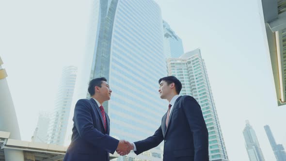 Asian businessmen partnership making handshake after deal in the city building in the background.