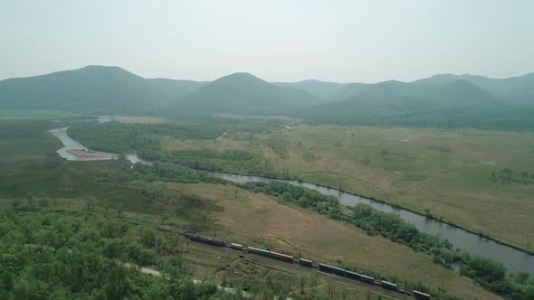 Aerial View of a Freight Train Passing By the Forest and a River