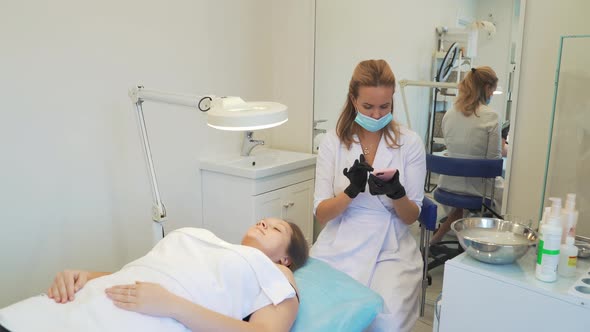 Cosmetologist in White Coat is Sitting in Office and Typing Text on Smartphone