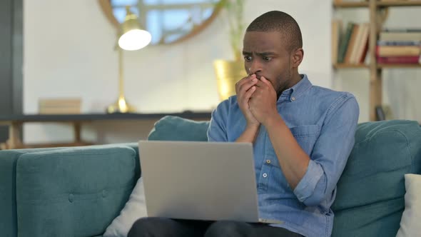 Young African Man with Laptop Reacting to Failure on Sofa
