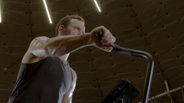 Low-angle Shot of Muscular Athlete Workout Air Bike Cardio in a Dark Gym 