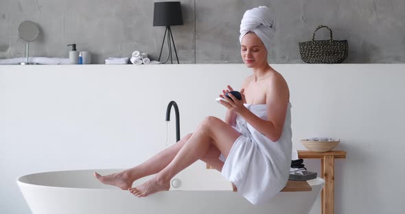 Delighted Halfnaked Pretty Woman White Bath Towels Applies Moisturizer to Her Legs Makes a Smoothing