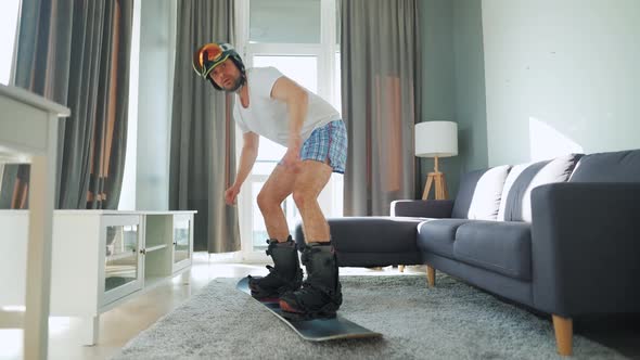 Fun Video. Man in Shorts and a T-shirt Depicts Snowboarding on a Carpet in a Cozy Room. Waiting for