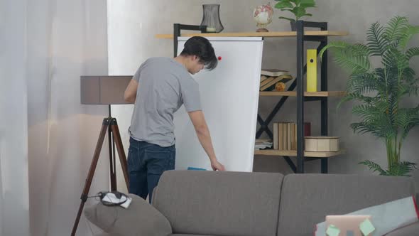 Asian Young Man Walking in Slow Motion to Whiteboard in Living Room and Writing with Marker