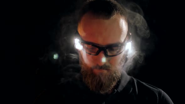 Young engineer with beard in protective goggles with backlight on black background