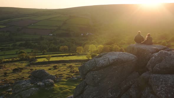 Young couple watching the sunset sitting on rock formations in Dartmoor national park moorland, Engl