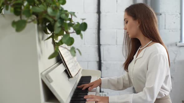 Side View of Attractive Young Woman Playing Gentle Music on White Classical Piano in Light Living