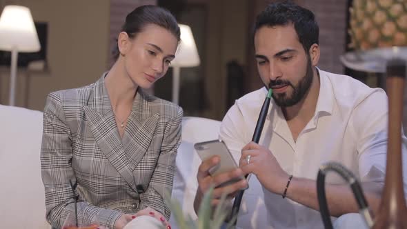 Man And Woman Smoking Shisha, Drinking Cocktails And Using Phone