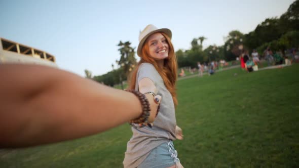 Caucasian Happy Redhaired Girl Walking in Park Holding Man By Hand Making Follow Me Story in Slow