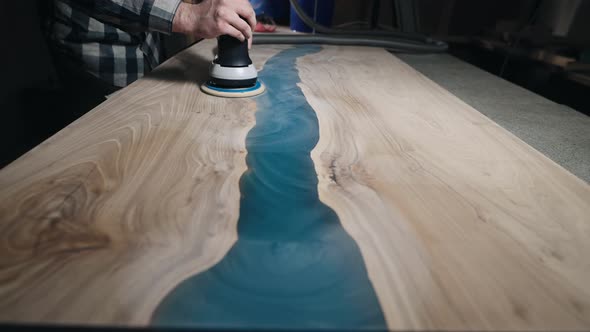 The Carpenter Processes the Surface of a Wooden Tabletop with a Grinder