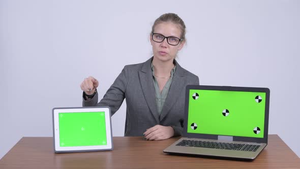 Young Beautiful Blonde Businesswoman Talking While Showing Laptop and Digital Tablet