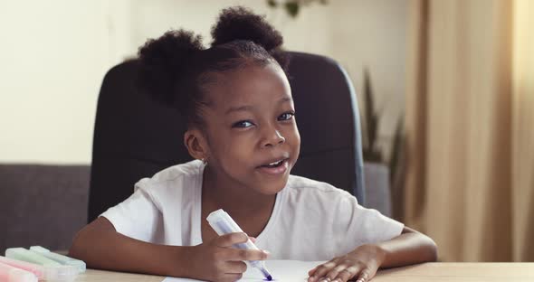Funny Little African Girl Speaks and Draws While Sitting at Table. Emotional Mixed Race Child Ethnic