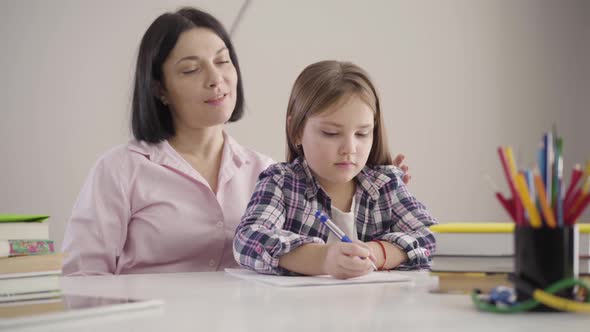 Portrait of Adult Caucasian Woman Sitting with Daughter at the Table. Parent Helping Schoolgirl with