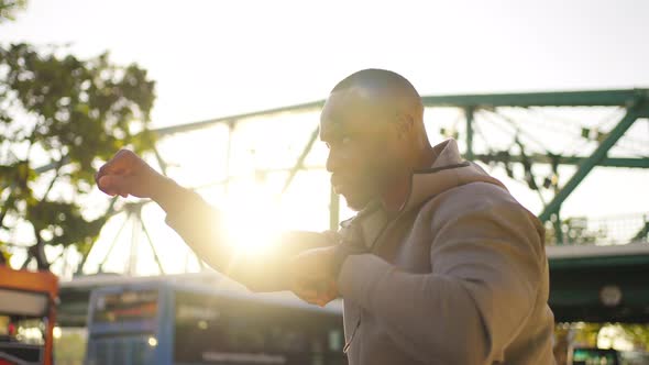 4K African man in sportswear do sport training boxing exercise in the city at summer sunset.