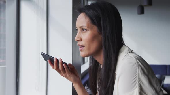 Smiling mixed race businesswoman standing talking on smartphone in office