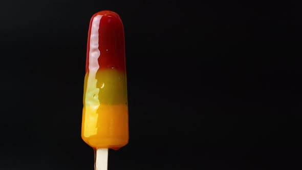 Multicolored rainbow ice cream melts on a black background. Ice cream on a stick on a hot summer day