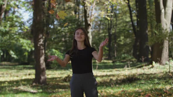 Girl Is Covering Her Face and Waving a Maple Tree Branch with Yellow Leaves in Autumn Park