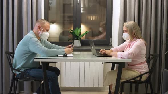 An Elderly Couple in Selfisolation Adult Man Sitting at a Desk and Using a Smartphone Adult Woman