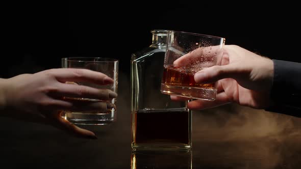 Two Hands with Glasses of Cognac Whiskey with Ice Cubes Making Cheers Toast on Black Background