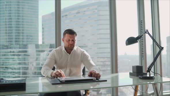 Young Business Man in Office at the Table. Cabinet in a Skyscraper. Male Businessman in a White