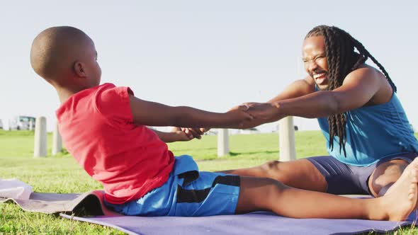 Video of happy african american son and father stretching on grass on sunny day