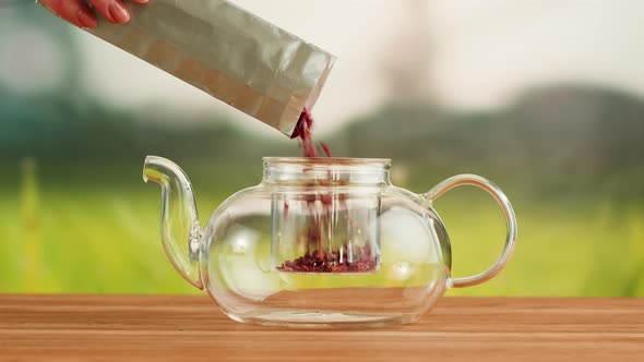 Putting Dry Tea Leaves Into Teapot on a Wooden Table