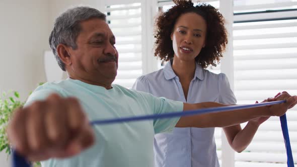 Mixed race female physiotherapist helping senior man exercise using exercise band