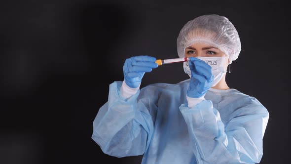 Girl Examines a Test Tube with Biomaterial. A Young Woman in Protective Clothing. On the Face of a