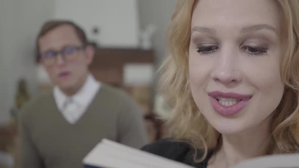 Portrait of Beautiful Blond Woman Reading Aloud the Book in the Foreground While Modestly