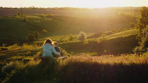 Mom with Son Are Resting Together on Nature at Sunset